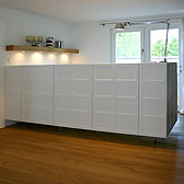 03 Planung: Tischlerei Kerber  _ Küchenblock und Sideboard mit weiss lackierten Kassetten _ Arbeitsplatte Edelstahl mit eingeschweißtem Becken und flächenbündigem Kochfeld _ Boden Eiche Massivdiele